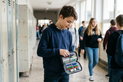Collégien ouvrant sa trousse scolaire colorée devant son casier dans un couloir d'école